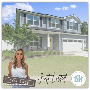 Image of a two-story house with blue siding and a yellow front door, featuring a 'Just Listed' banner and a logo for 'The Stevie Hahn Team' in the bottom right corner. A smiling woman is holding a 'For Sale' sign at the bottom left